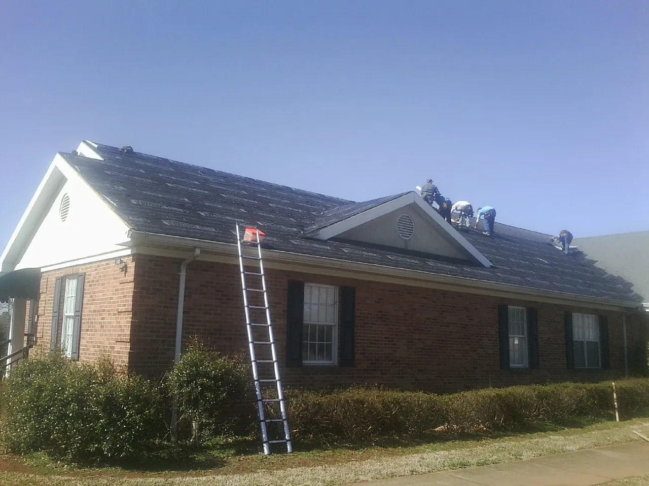 Crew tearing shingles off a brick ranch roof with a ladder set — Metal Roof Repair work by our crew in Stockertown