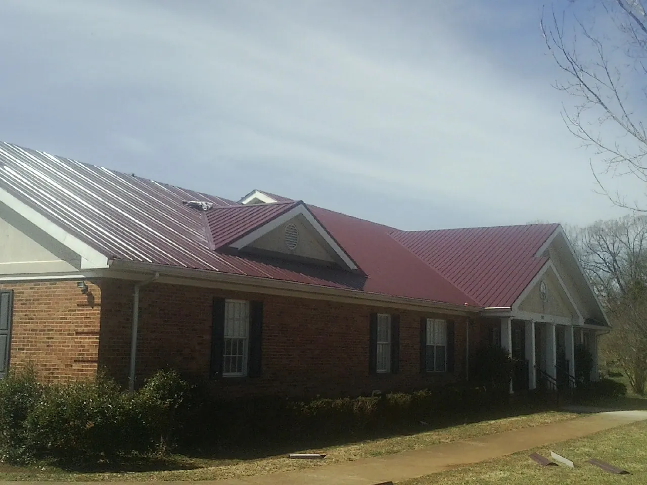 Red metal roof with gabled entries on a long brick building, from a Hail Damage Roof Repair job in Stockertown