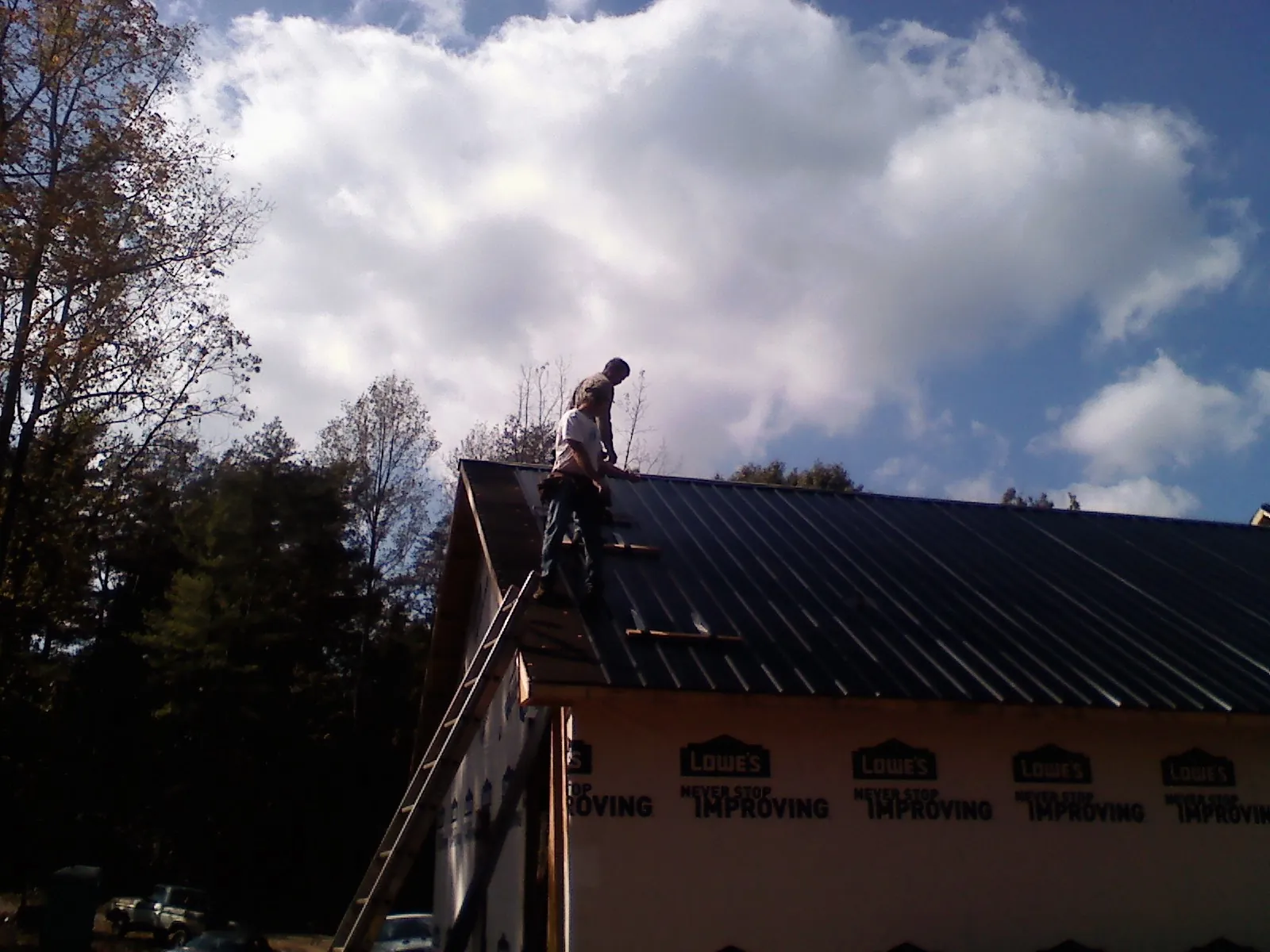 Roofer fastening dark metal panels high against a cloudy sky, from a Roof Inspection job in Stockertown