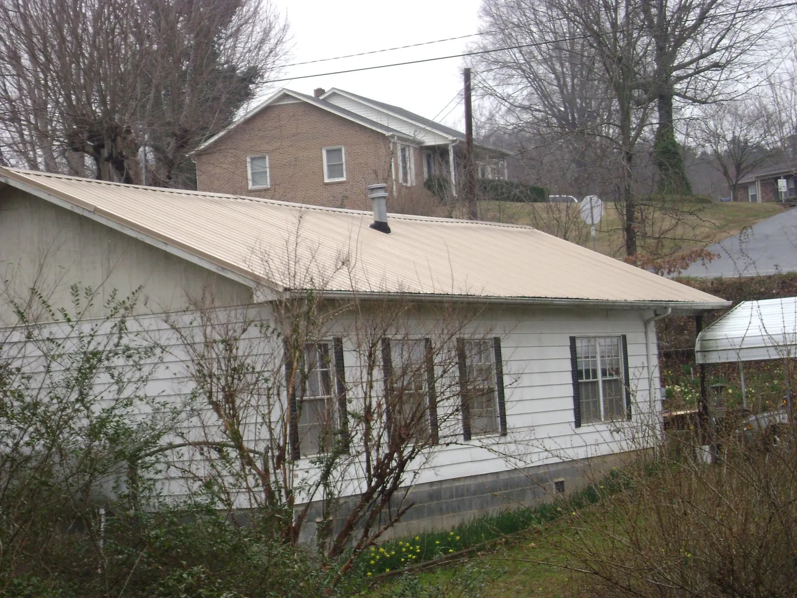 Tan metal roof on a white sided house set into a hillside — Commercial Roofing by Roofing Brothers in Stockertown